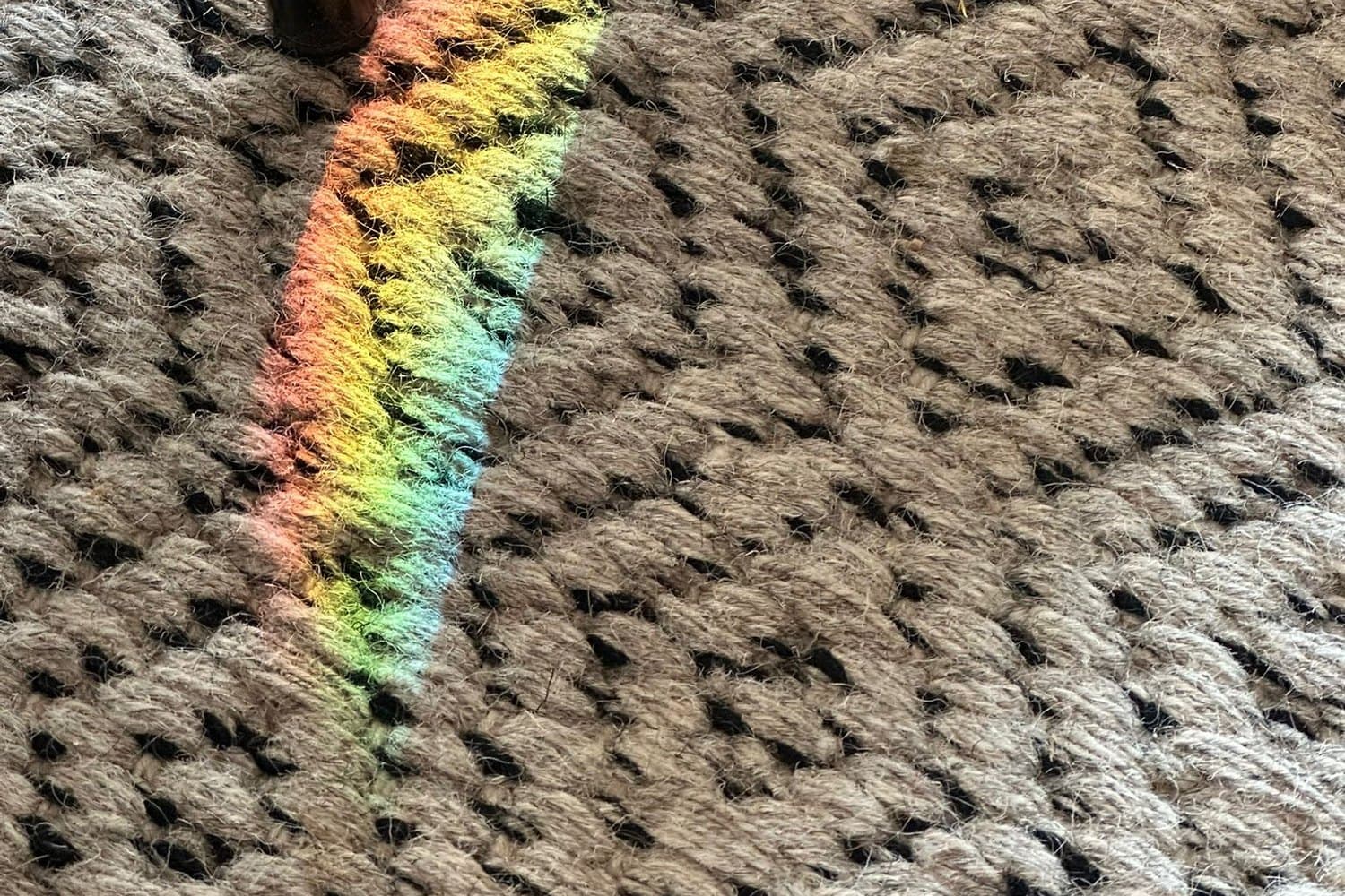 Un trait d’arc-en-ciel en diagonale sur un tapis de laine tressée.