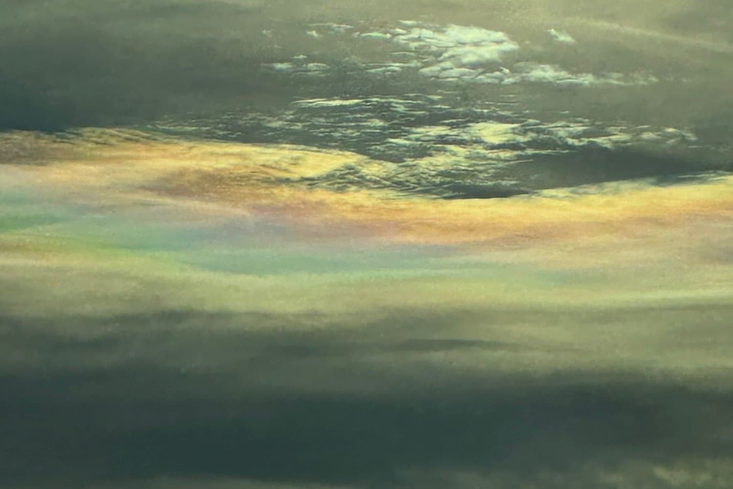 Une bande de nuages irisés aux couleurs pastel, sous un ciel voilé.