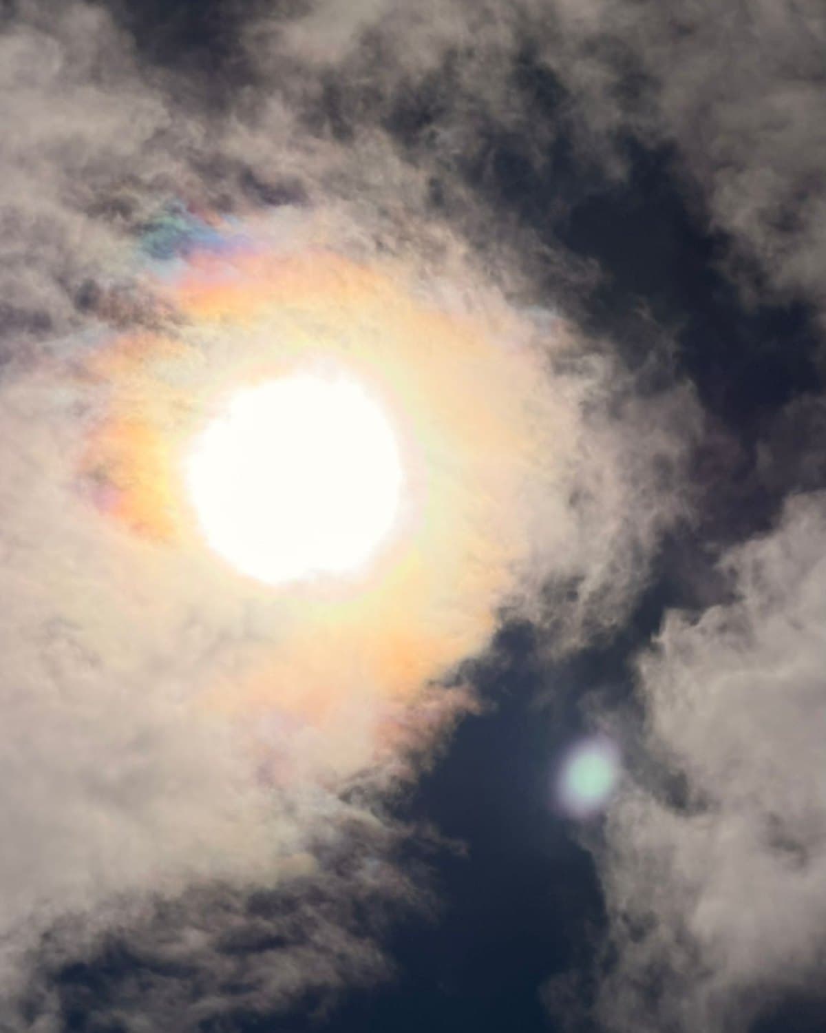 Le soleil entouré d’un halo irisé, entre des nuages sombres.