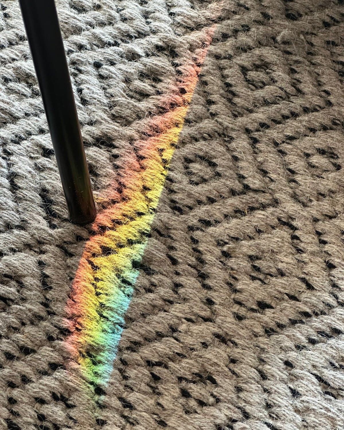 Un trait d’arc-en-ciel posé en diagonale sur un tapis de laine tressée, au pied d’un lampadaire.