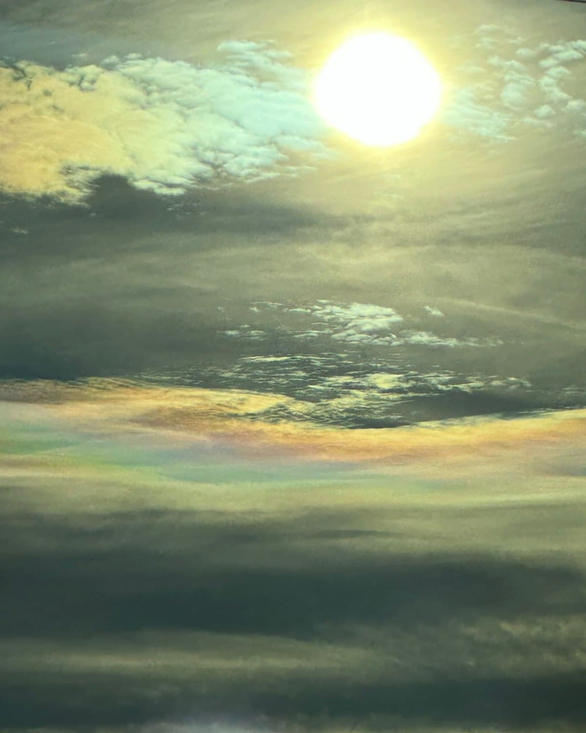Le soleil au-dessus d’une nappe de nuages irisés, aux couleurs pastel.